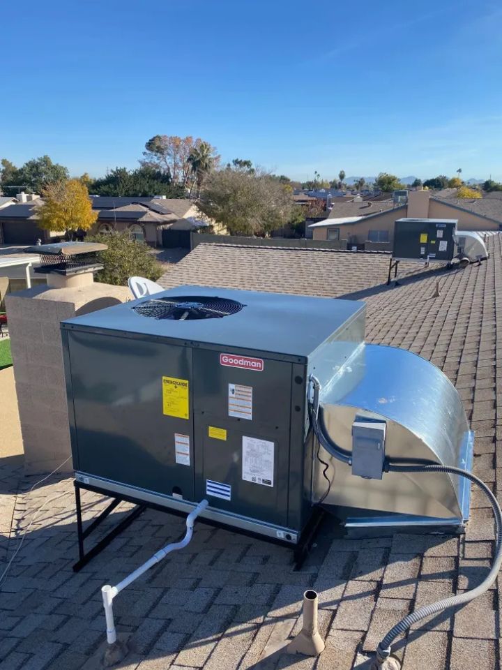 lacp-img-23 Goodman rooftop HVAC unit installed on a sloped roof, with clear blue sky and residential neighborhood in the background.